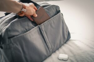 Hand placing a brown travel wallet into a gray soft-sided bag — ideal for documents on a first time yacht charter packing list