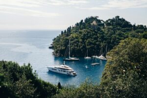 Luxury yacht and sailing boats anchored in a scenic bay near Portofino, Italy with lush green hills in the background