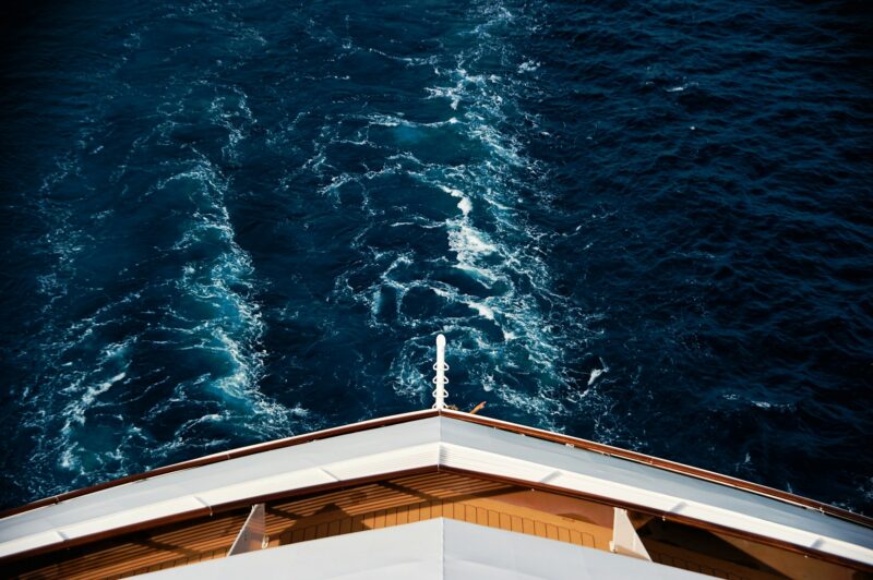 the bow of a yacht cruising through deep blue water with a visible wake, viewed from above