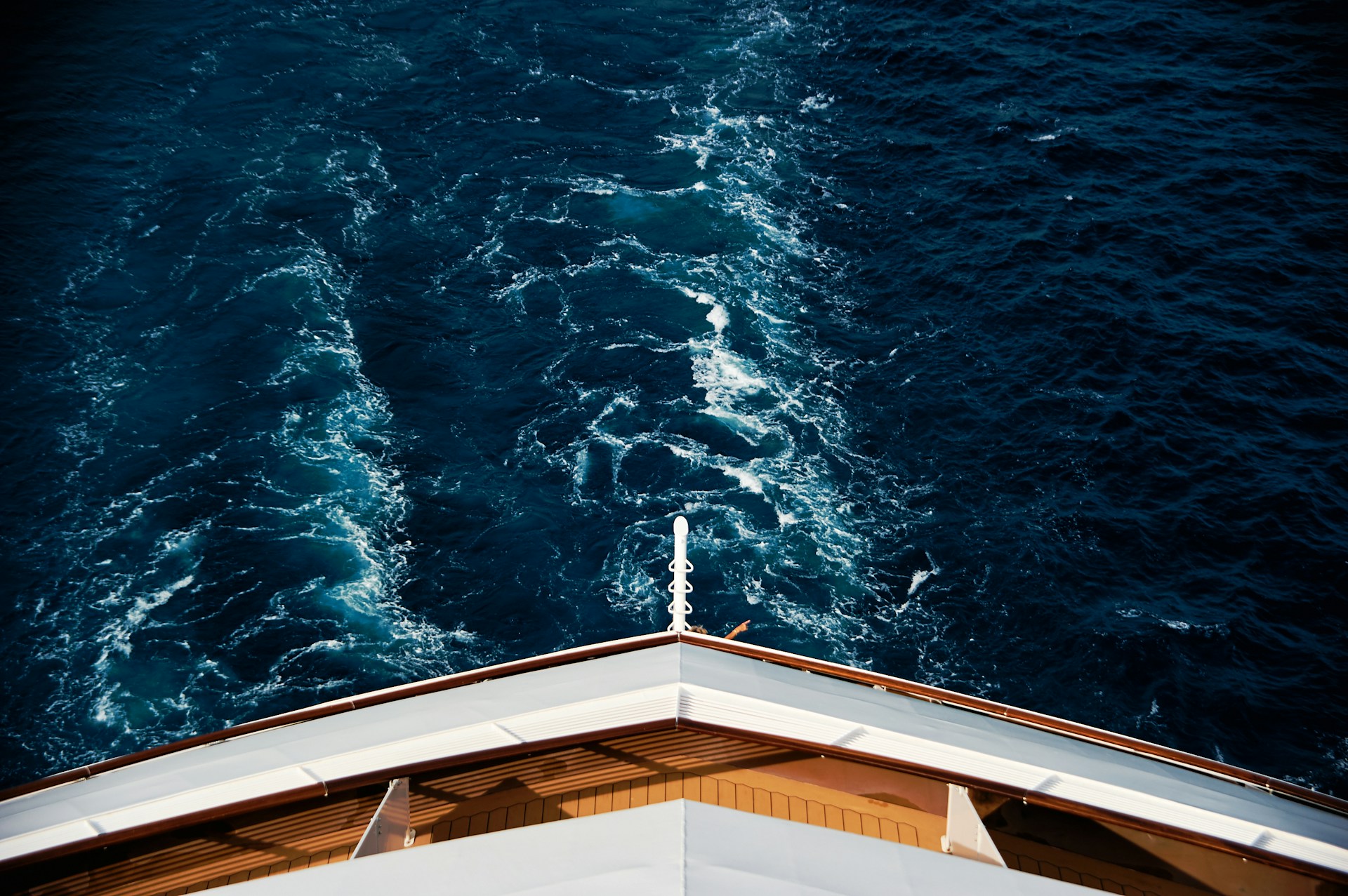 the bow of a yacht cruising through deep blue water with a visible wake, viewed from above